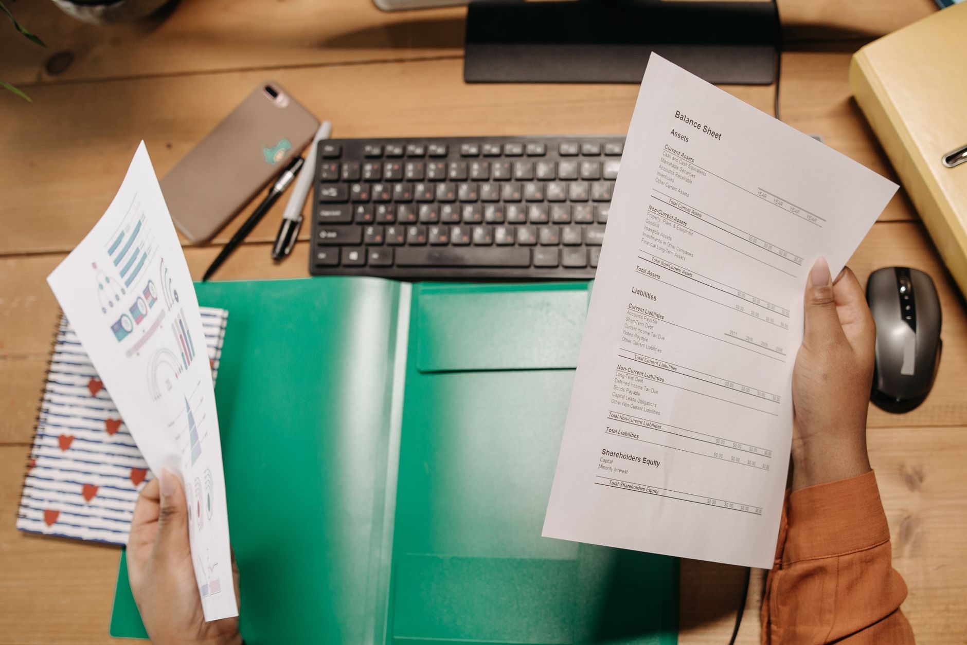 Hands holding printed documents over an open green folder on a desk