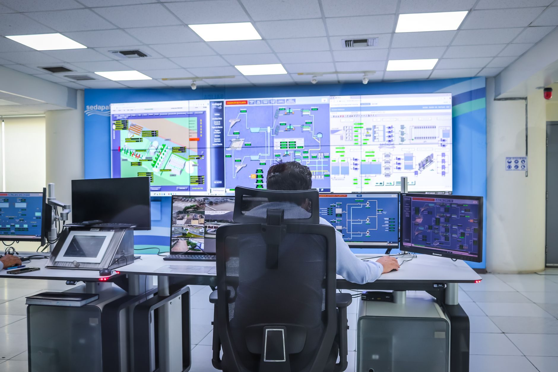 A pipeline controller at a console in front of a large wall of SCADA screens in a modern control room