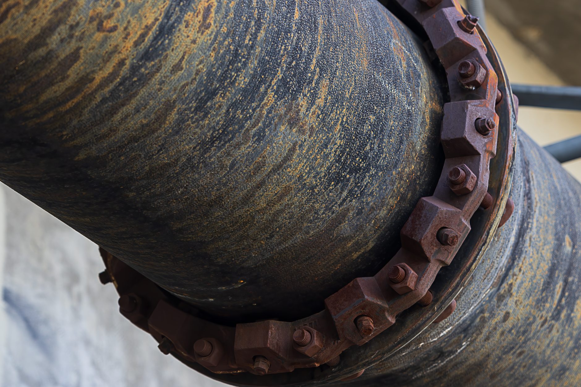 A weathered steel pipeline with a rusted bolted flange running across rocky ground