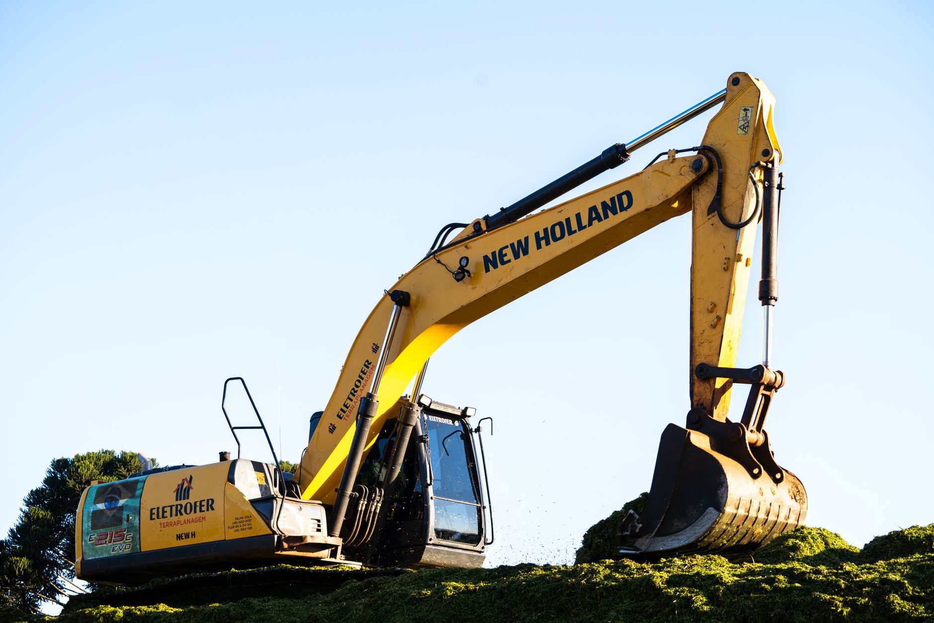A yellow excavator with its arm raised against a clear evening sky