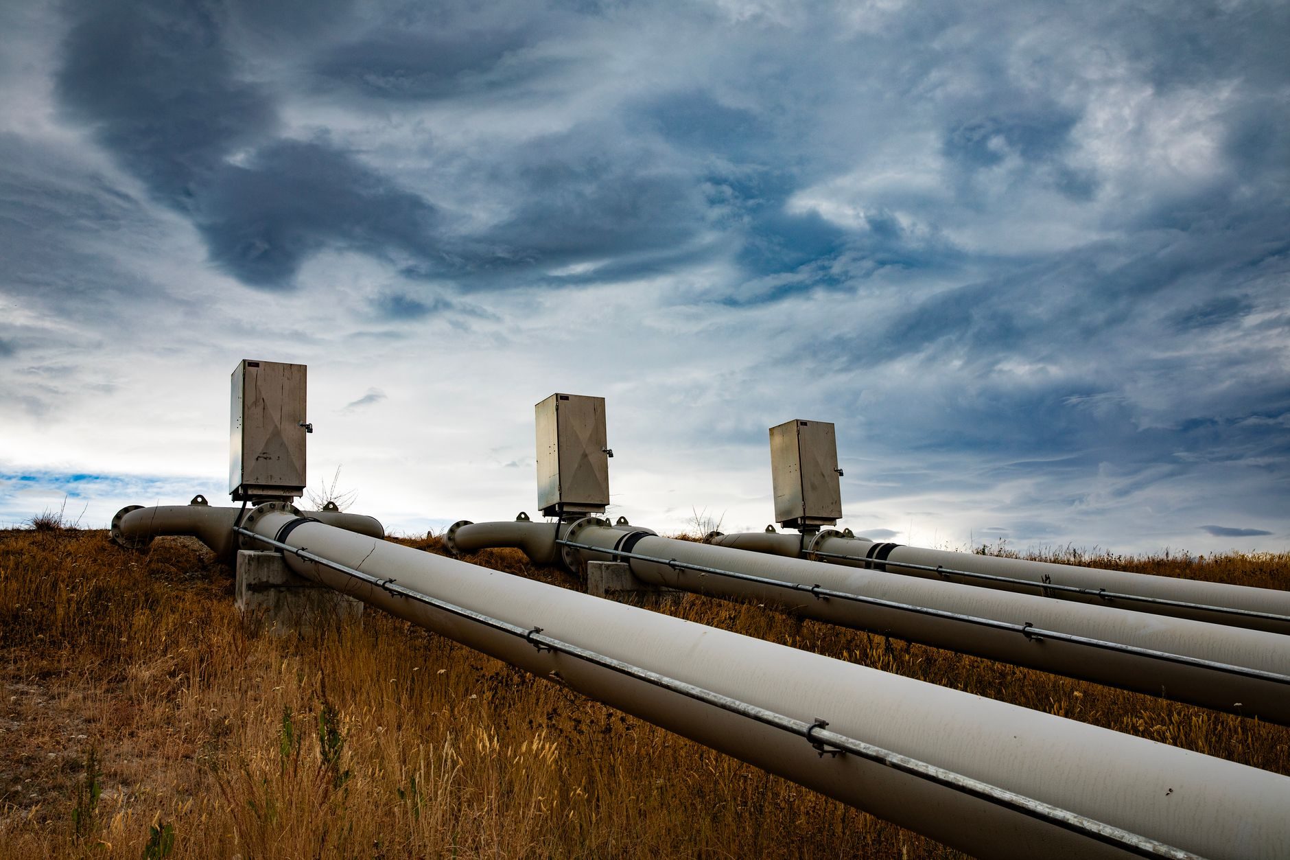 Pipelines with risers crossing an open field under a stormy sky